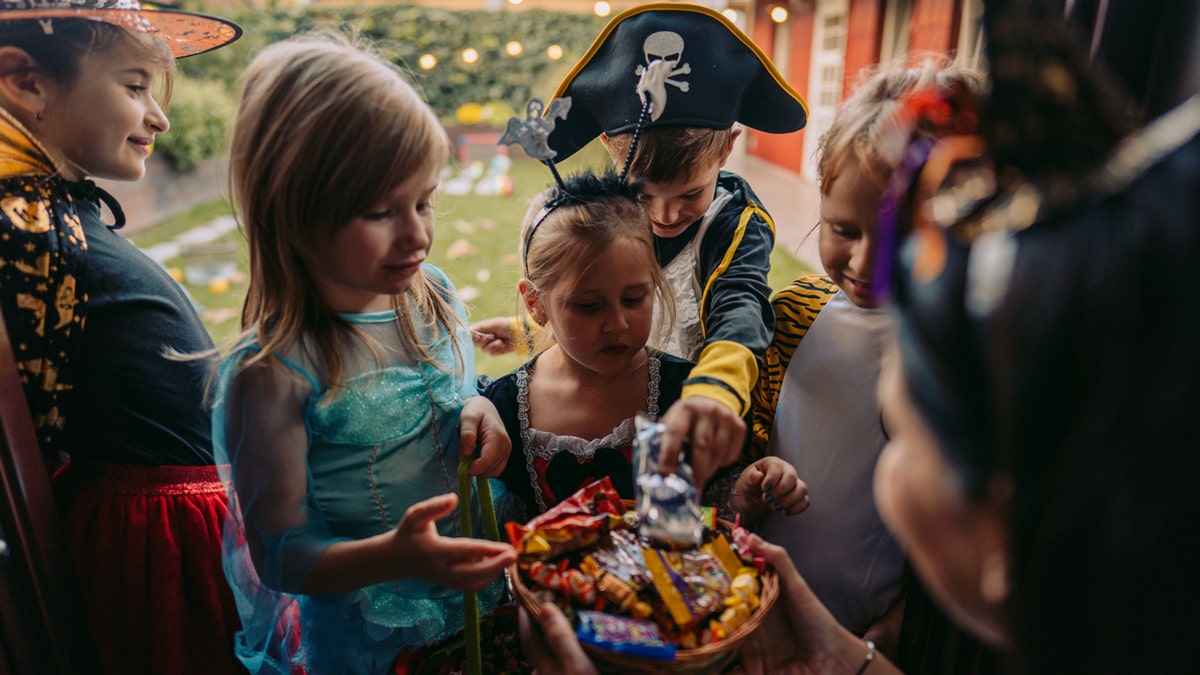 Children pick from a bowl of candy while trick-or-treating on Halloween.