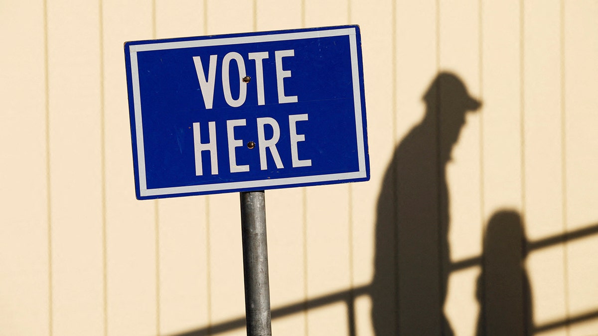 vote here sign with shadow of person walking by in background