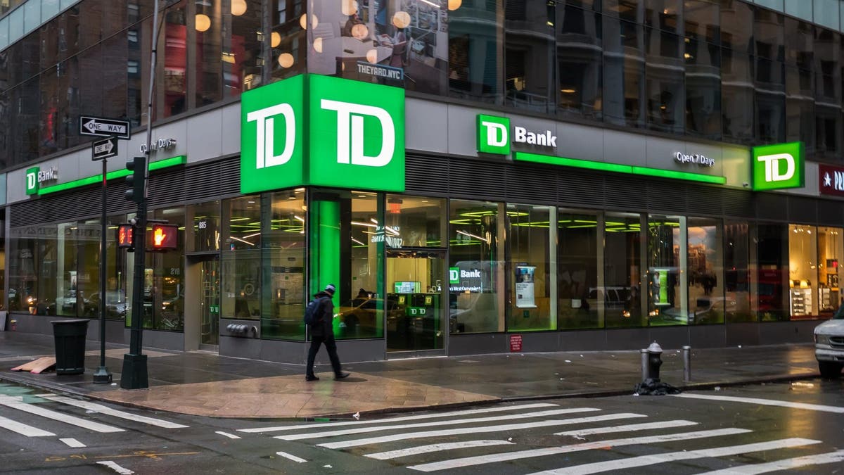 TD Bank in NYC ictured on a rainy day with few people walking on the sidewalk, dim lighting