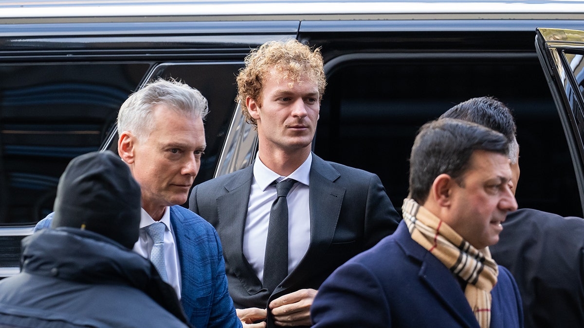 Daniel penny buttons his suit jacket as he walks up to court, flanked my his legal team and supporters