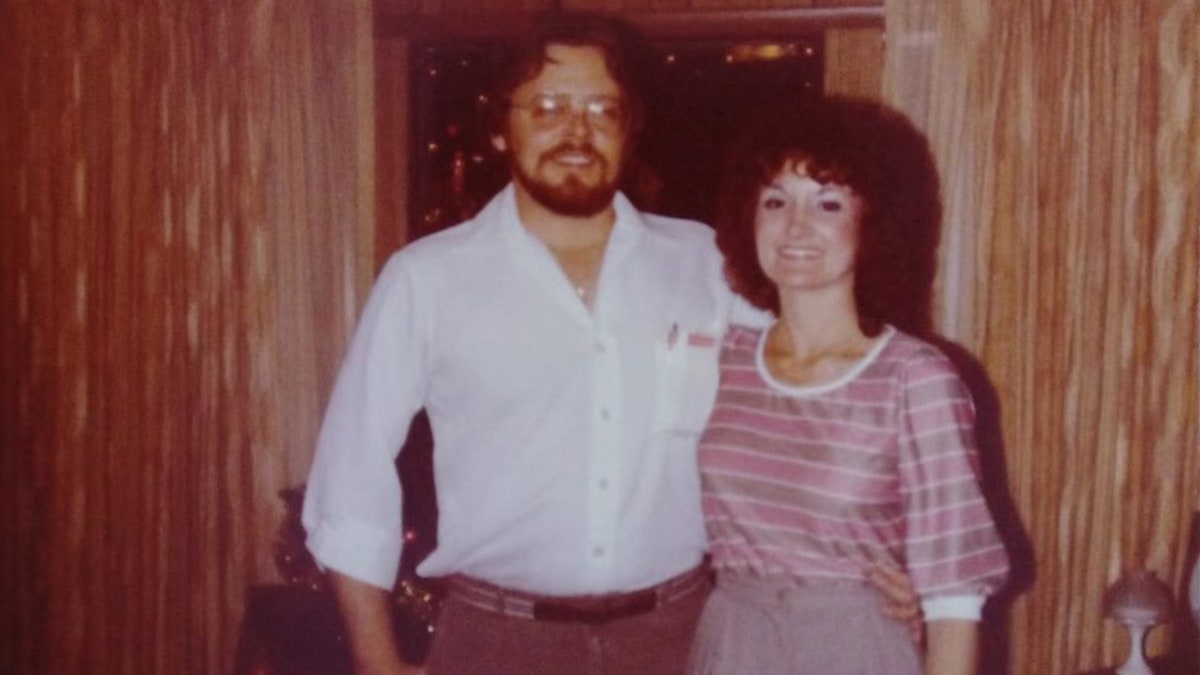 Wanda Holloway in a striped shirt and skirt posing next to her ex-husband wearing a white shirt and smiling.