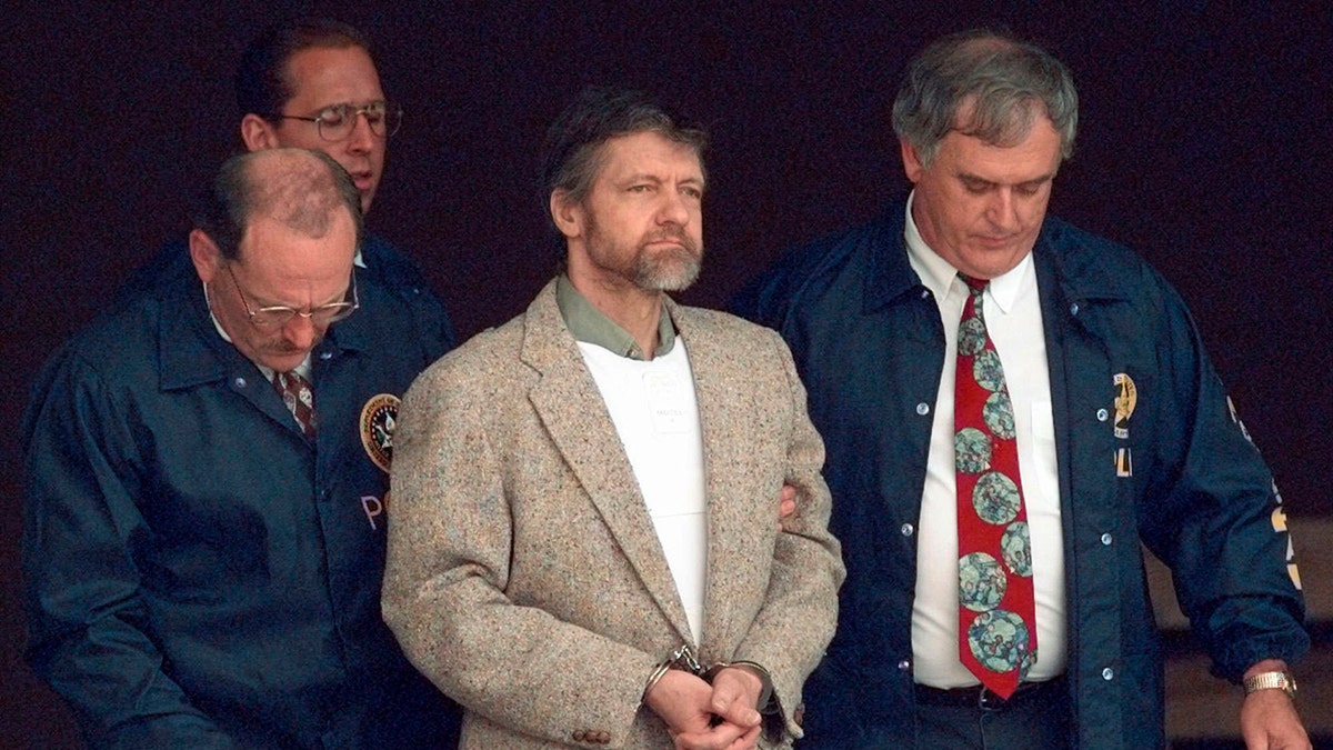 Unabomber wearing a tan jacket over a flak vest as he is escorted in a prison transfer