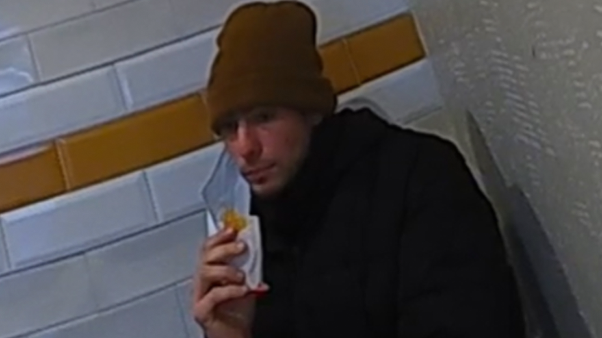 mangione eating a mcdonalds hashbrown with mask hanging from one ear